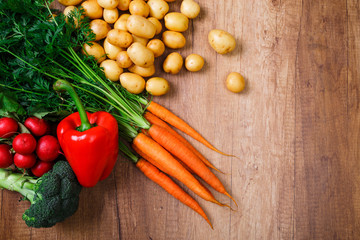 Potatoes with carrot and pepper. Red radish, brocoli and raw new potato. Fresh natural vegetables. Organic bio food. On wooden table.