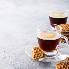 Glass cups of coffee with mini stroopwafel, syrupwaffles cookies on light gray background with copy space.
