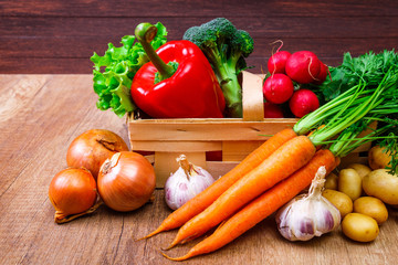 Vegetables. Potatoes, carrot and red pepper. Lettuce salad, garlic and brocoli. Onion and radish. Wooden basket on rustic table.