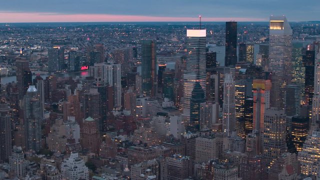 AERIAL HELI SHOT: Huge shining glassy skyscrapers, lit contemporary office buildings and luxury condo towers rising above low-rise blocks of flats in Midtown Manhattan New York City at pik light dawn