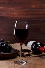 Red wine. Bottle with wineglass. Dark grapes branch on plate. On rustic wooden background.
