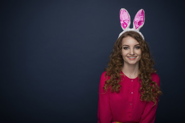 Cheerful beautiful woman in a red shirt and with rabbit ears on a dark blue background.