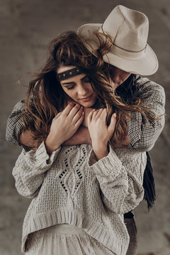 Strong cowboy man in white stylish hat hugging beautiful brunette hipster girl from behind