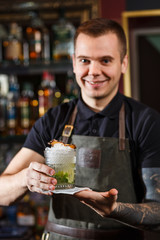 Cheerful bartender gives the cocktail to customer.