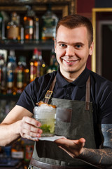 Cheerful bartender gives the cocktail to customer.