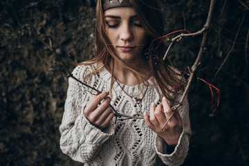 stylish hipster woman posing in knitted sweater holding branch with berries. atmospheric sensual moment. boho country fashionable look.