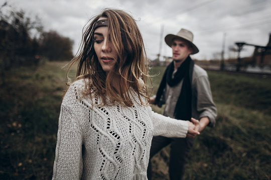 stylish hipster couple holding sensually hands. boho gypsy woman and man in hat embracing in windy field. atmospheric motion moment. fashionable look. rustic wedding concept