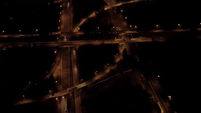 AERIAL HELI SHOT Flying above two level stack interchange road junction on expressway highway with on-ramp and off-ramp for traffic to pass through. Cars, trucks & trailers traveling along the freeway
