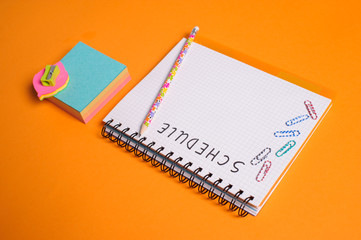 Top view of office tools with blank notebook on orange background