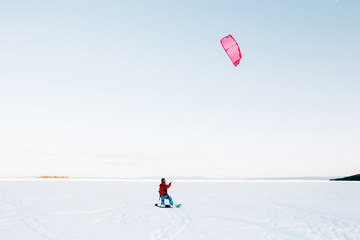 Fototapeta na wymiar Snowboarder with a kite rides on a frozen lake on free ride. Kola Peninsula, Russia