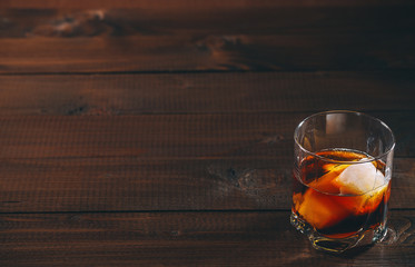 Cola with cognac or rom in glass and ice cubes on wooden table. Free space