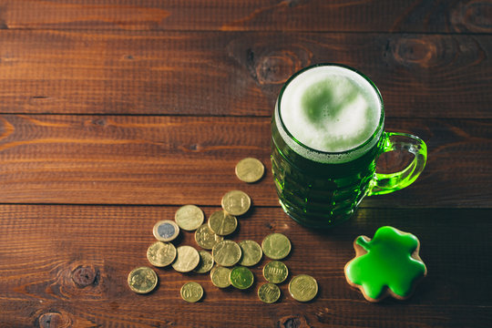 Beautiful background for St. Patrick's day with a glass of green beer, gold coins and gingerbread clover on a wooden table. Free space