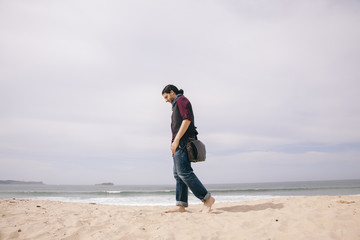 caucasian hipster man walking alone on the beach with casual clothes