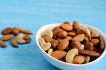 White bowl of nuts, almonds, walnuts, pistachios, cashew, hazelnuts. Blue wooden background