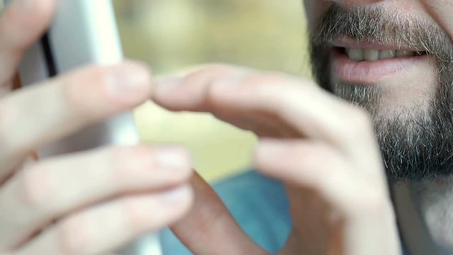 Man with beard looks happy while browsing internet on smartphone, close up, steadycam shot
