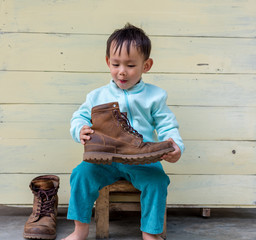 Asian baby boy try to wearing father boots while drinking milk from bottle
