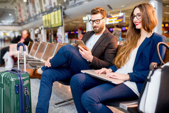 Elegant business couple working with laptop and phone sitting at the waiting hall in the airport. Business travel concept