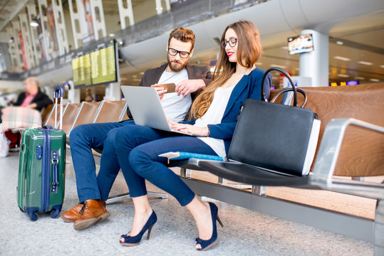 Elegant business couple working with laptop and phone sitting at the waiting hall in the airport. Business travel concept