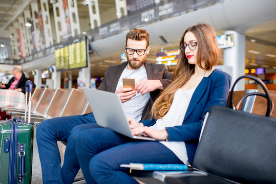 Elegant Business Couple Working With Laptop And Phone Sitting At The Waiting Hall In The Airport. Business Travel Concept