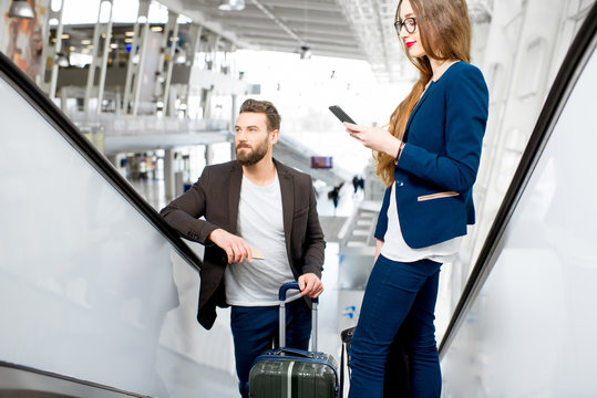 Business couple getting up with baggage on the escalators at the airport. Business travel concept