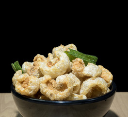 Crispy pork rind in black bowl isolated black background