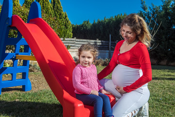 happy pregnant mother with toddler on slide playground area