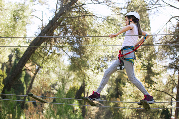 Happy school girl enjoying activity in a climbing adventure park on a summer day