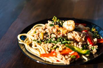 Drunken noodles seafood spaghetti in gray dish on wooden table.