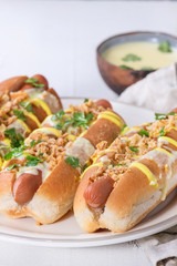 Hot dogs with sausage, fried onion, coriander leaves, cheese sauce and mustard, served on white ceramic plate with textile over white concrete texture background. Fast food. Close up