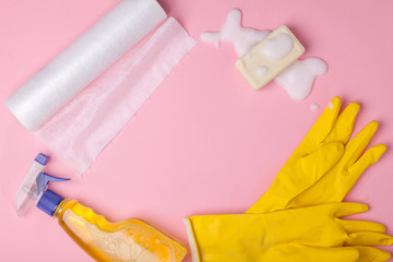 duster rags, yellow rubber gloves, detergent, soap in foam around blank copy space isolated on pink background, flat lay