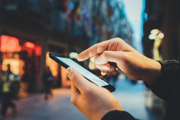 Closeup of male hands using smartphone with blank screen, horizontal image of young man holding modern cellphone while walking at evening city streets