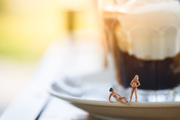 Miniature people in swimsuit relaxing on glass of iced coffee. Summer concept.