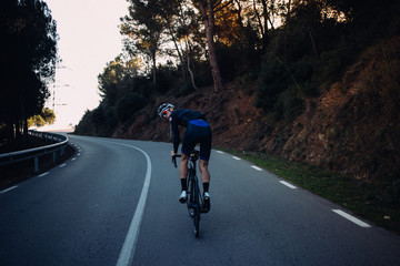 Fototapeta premium A fit young man riding his bicycle on a dark sunset road looks back at the camera
