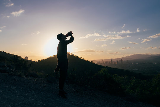 Silhouette of a young sexy man quenching his thirst in the sunset in the mountains after sport