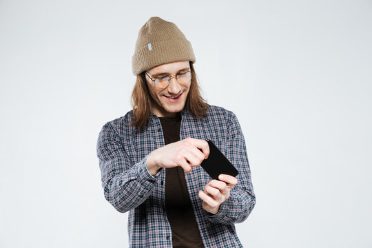 Smiling hipster in eyeglasses playing on smartphone