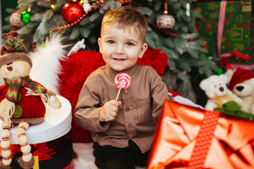 Stylish boy in brown shirt sits before Christmas tree