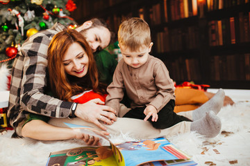 Mother, father and little son read book lying on fluffy carpet