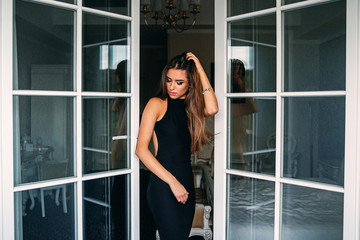 Fototapeta na wymiar Attractive charming sexy girl in stylish black dress in hotel room near the door of balcony