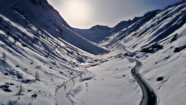 Beautiful winter aerial flight of a drone over the valley in mountains. Scenic sunset. Ski route and road are going parallel to each other along the valley. Solden, Austria