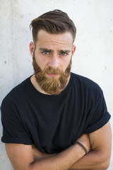 Bearded man posing in the street with crossed arms.