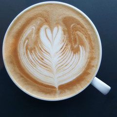 Top view of a mug of latte art coffee on black background.