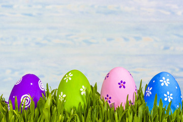 Pastel colored easter eggs in green grass over rustic wooden background.