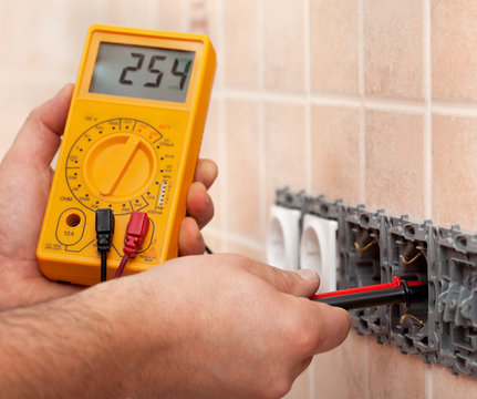 Electrician hands measuring voltage in electrical wall socket with multimeter