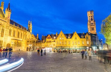 Naklejka premium BRUGES, BELGIUM - MARCH 2015: Tourists visit ancient medieval Burg Square at night. Brugge attracts more than 2 million people annually