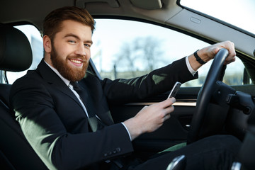 Smiling handsome business woman using phone while sitting in car