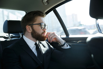 Man in eyeglasses sitting at the back seat of car