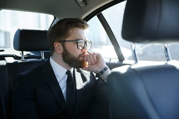Man in eyeglasses sitting at the back seat of car