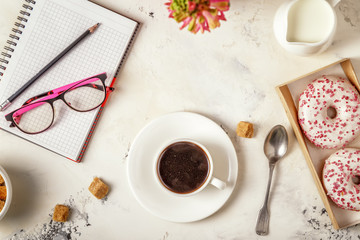 Notepad, donuts and coffee on white table.