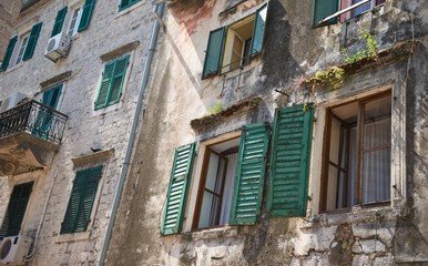 Fototapeta na wymiar Old Mediterranean house and facade in the town of Kotor, Montenegro. Walls of building, windows with open and closed shutters. Climate control air-conditioning 