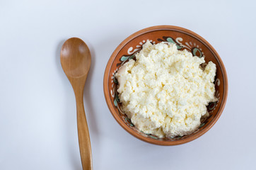 fresh cottage cheese in a plate with a wooden spoon on a white background